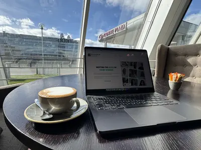 The Educamus Tuition website open on a laptop at a table in Glasgow, with the BBC Scotland building and the Crowne Plaza visible across the Clyde